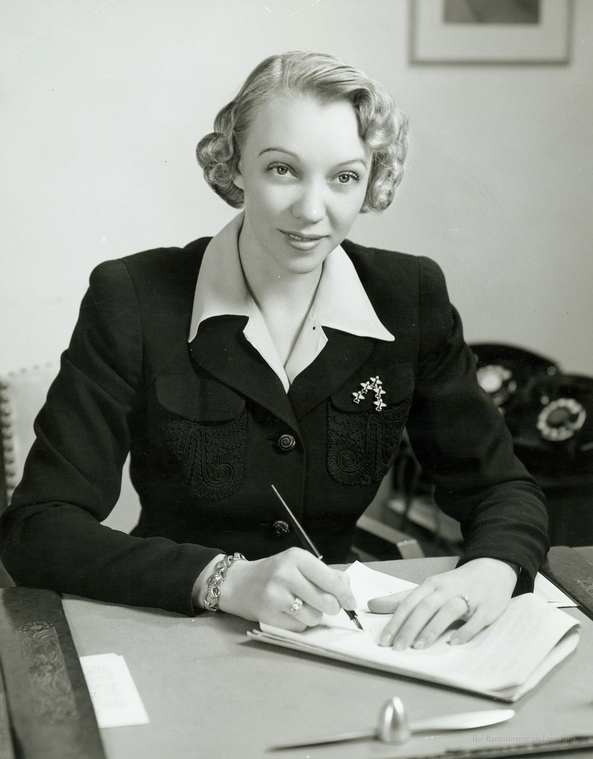 Olive Ann Beech seated at a desk, writing with a pen