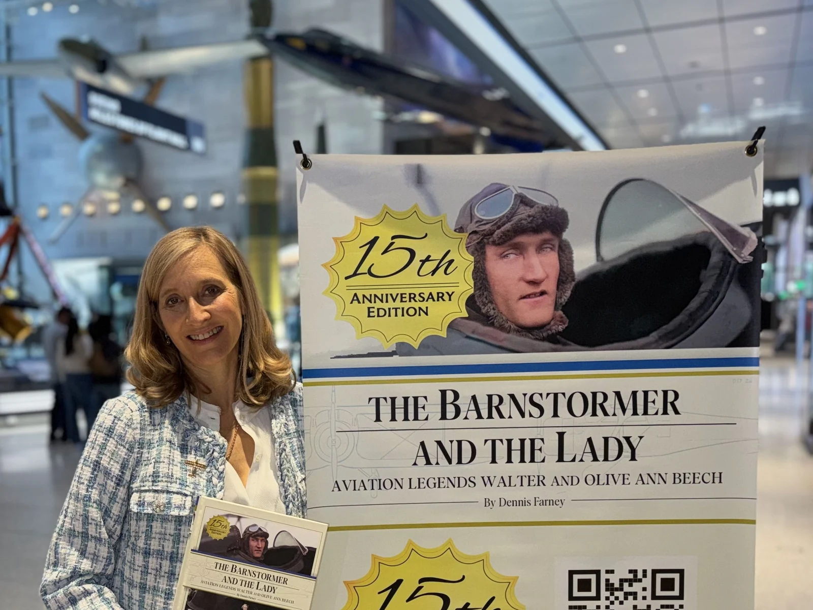 Jennifer Pitt holding the book beside a banner for The Barnstormer and the Lady in a museum hall
