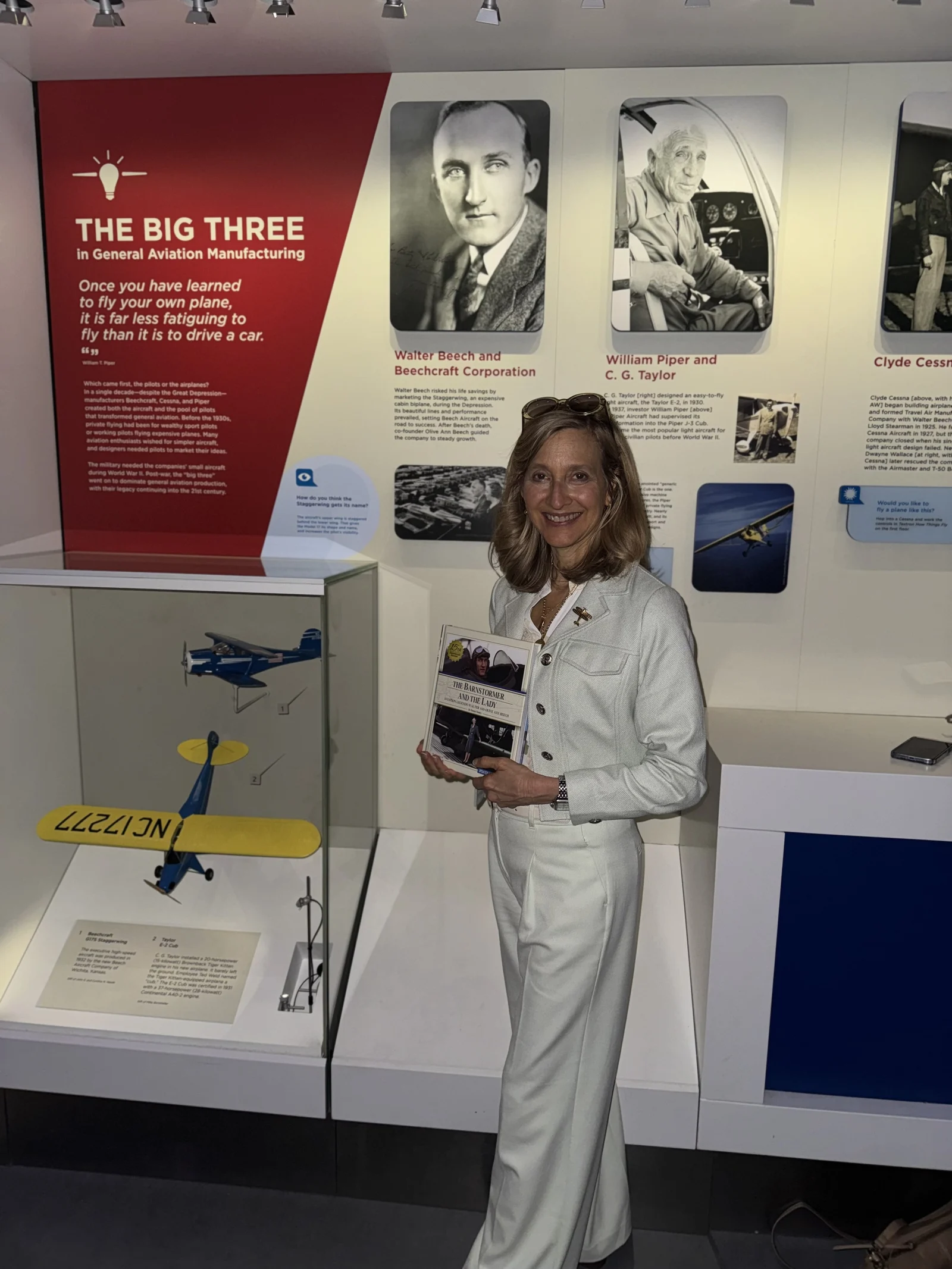 Jennifer Pitt holding the book in front of a museum display on general aviation manufacturers