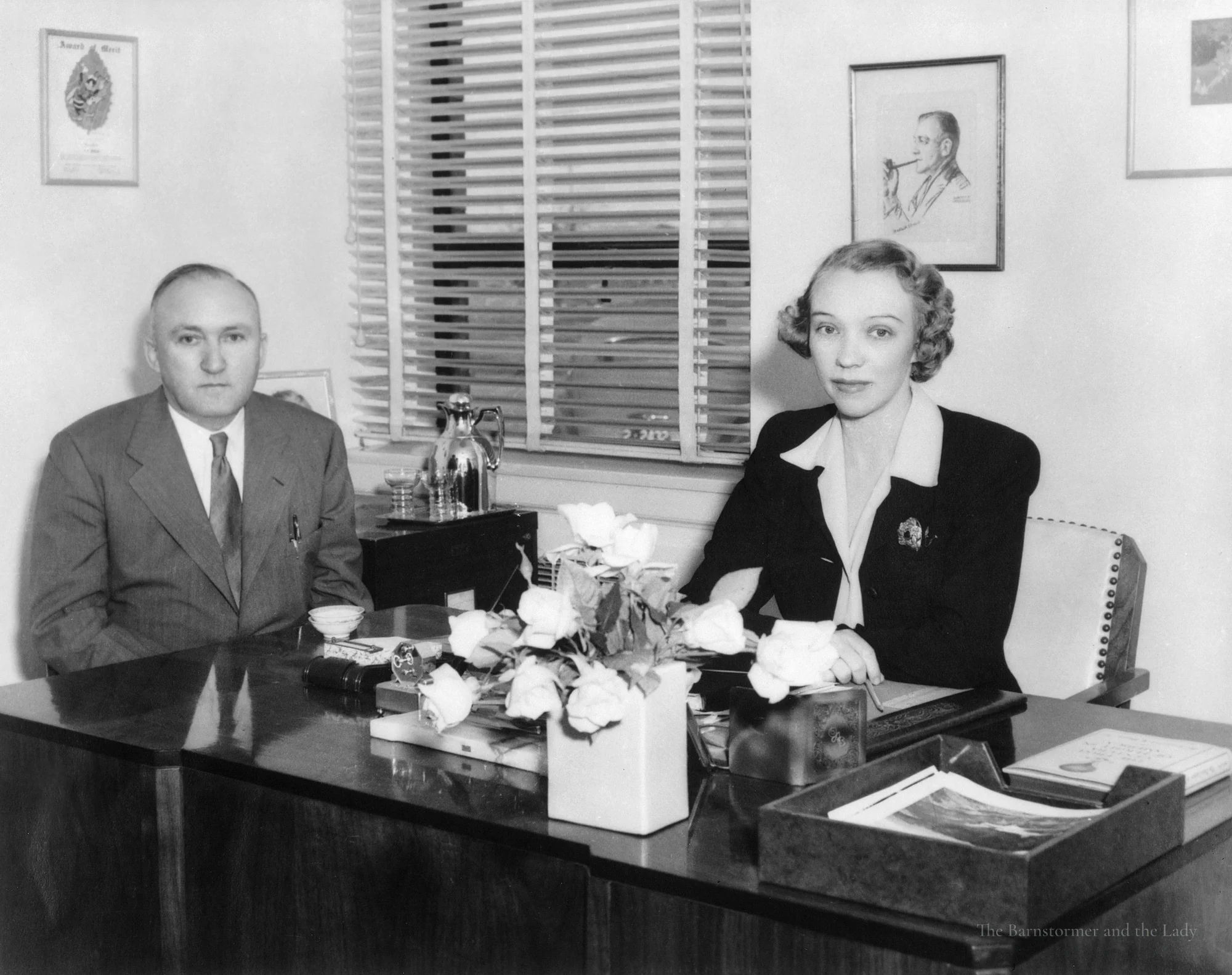 Walter and Olive Ann Beech seated at a desk with a vase of white roses