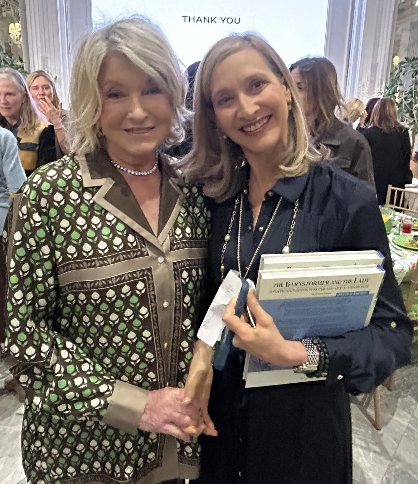 Jennifer Pitt, holding the book, with Martha Stewart in an event hall with set tables