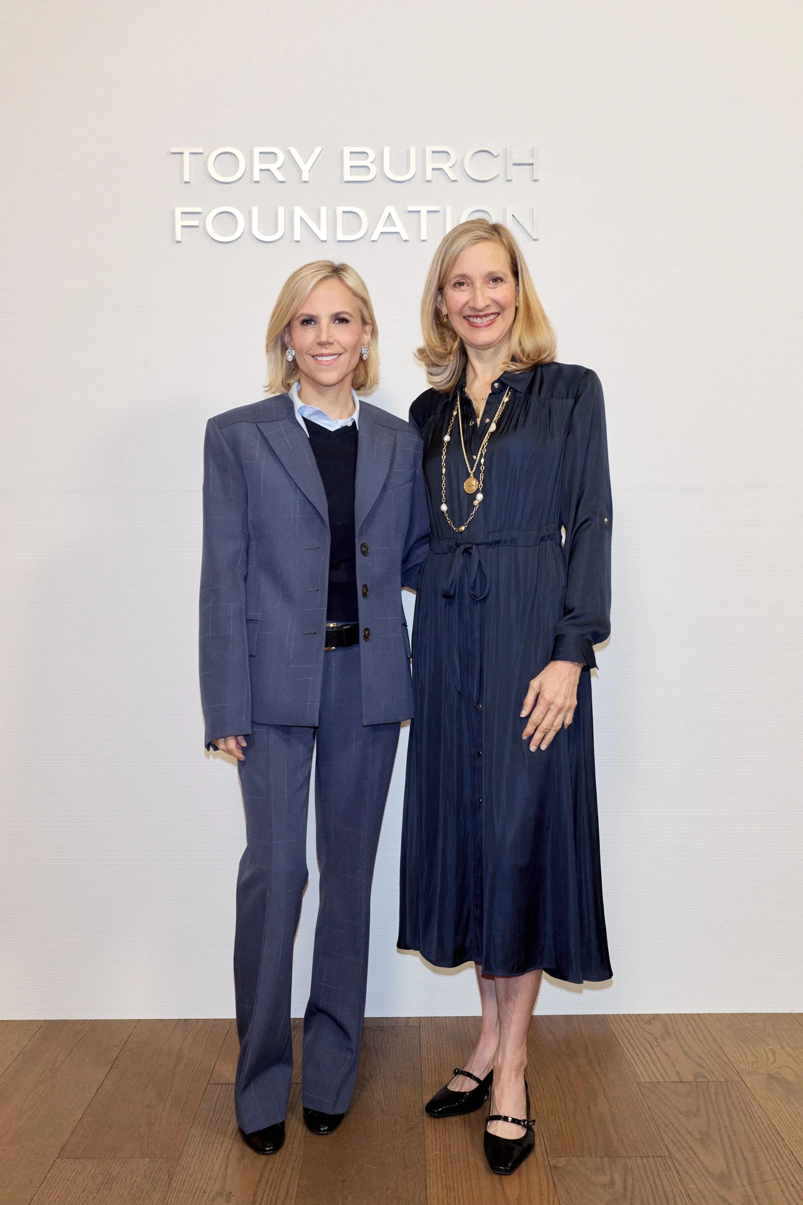 Jennifer Pitt and Tory Burch standing before a wall lettered Tory Burch Foundation