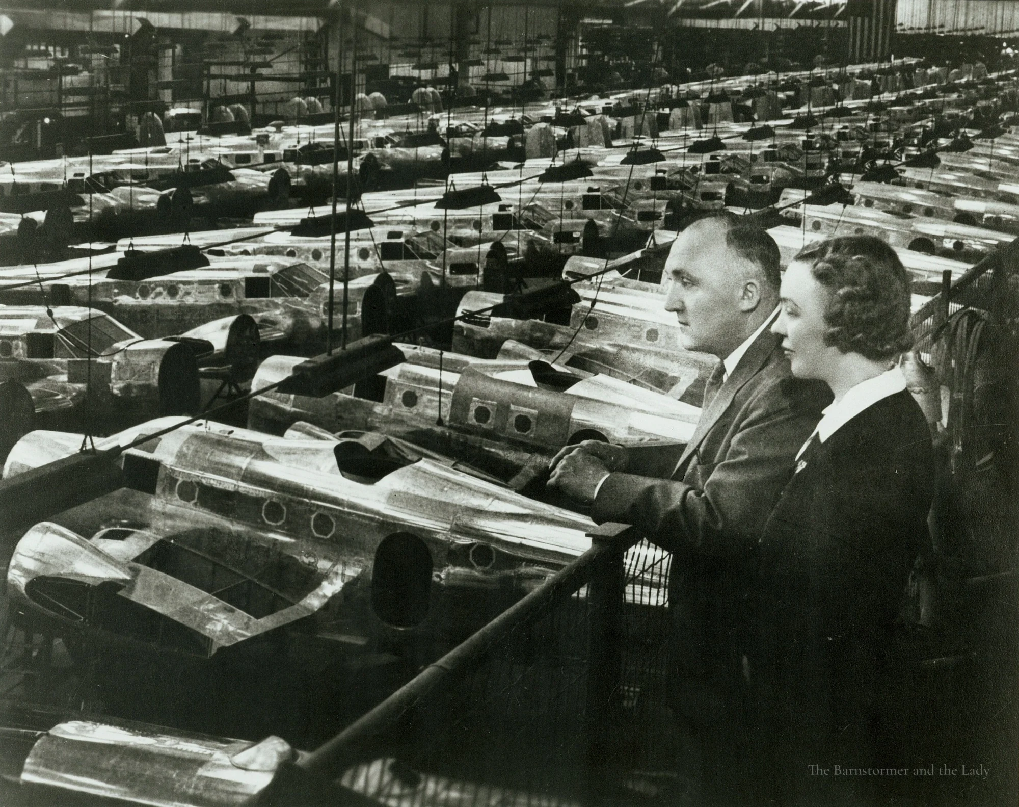 Walter and Olive Ann Beech looking out over rows of aircraft fuselages on a factory floor